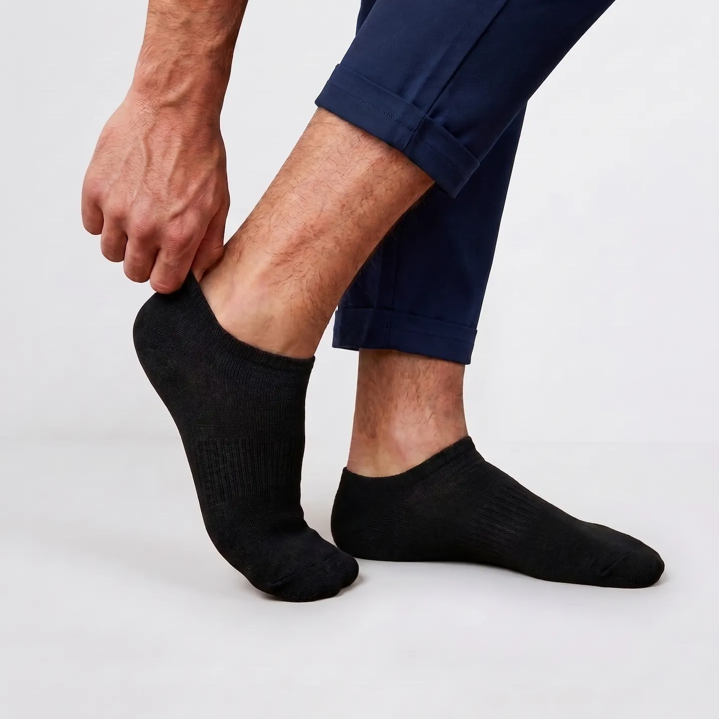 Man wearing navy blue trousers putting on a clean, Oeko-Tex certified black cotton no show sock free of manufacturing residue.