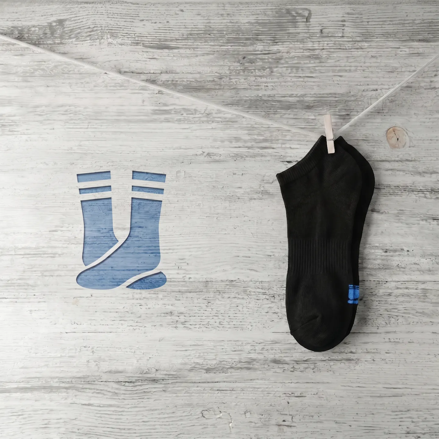 Pair of clean black cotton no show socks hanging from a wooden clothespin against a weathered fence.